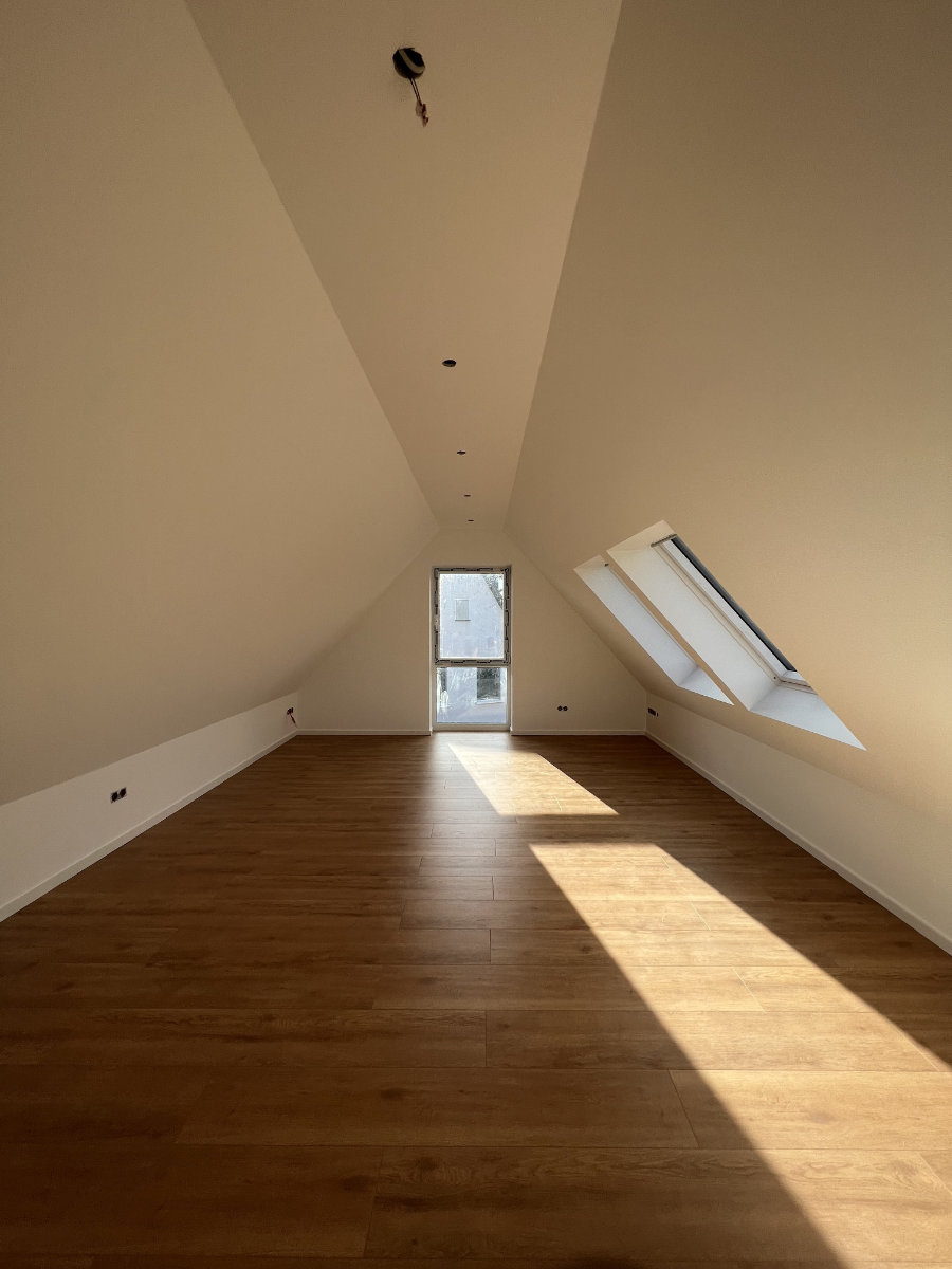 Ausgebauter Dachboten mit hellen Fenstern, Holzboden und weißen Wänden