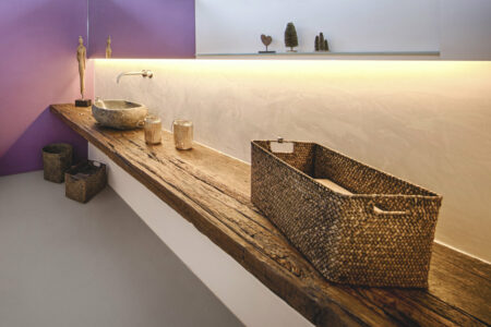 Altes Holzbrett im Badezimmer auf dem ein Waschbecken, eine Statue und mehrere Körbe mit Handtüchern stehen