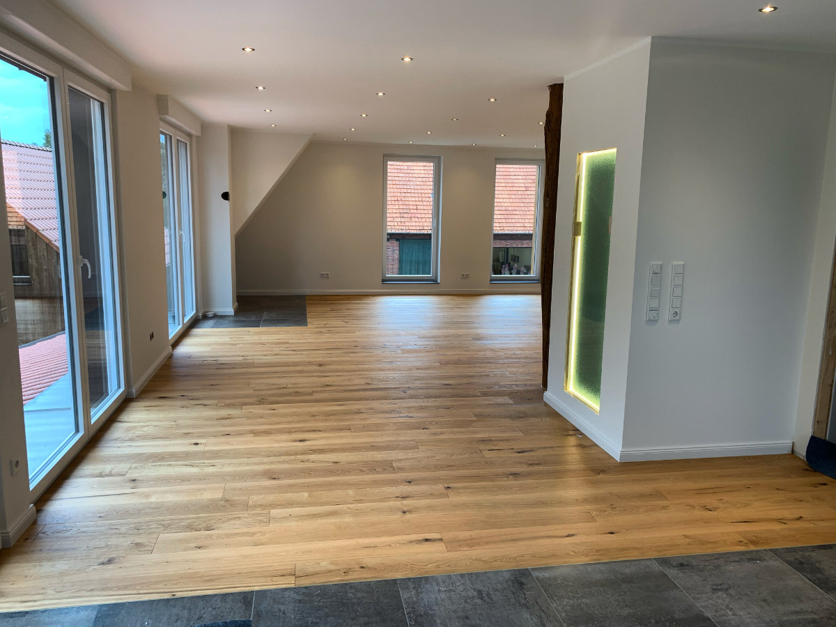 Moderne Räumlichkeiten im Dachgeschoss mit weiß gestrichenen Wänden und einem Übergang von Holzfußboden zu grauen Fliesen